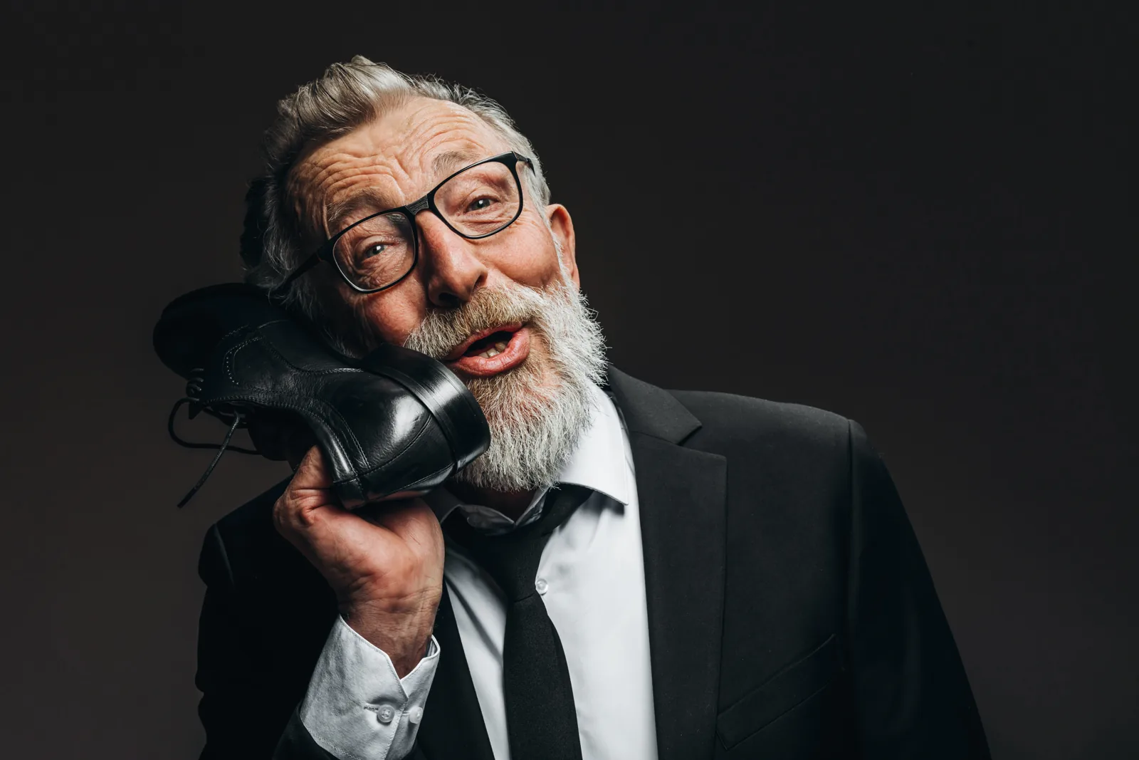 A man playfully holding a shoe to his ear